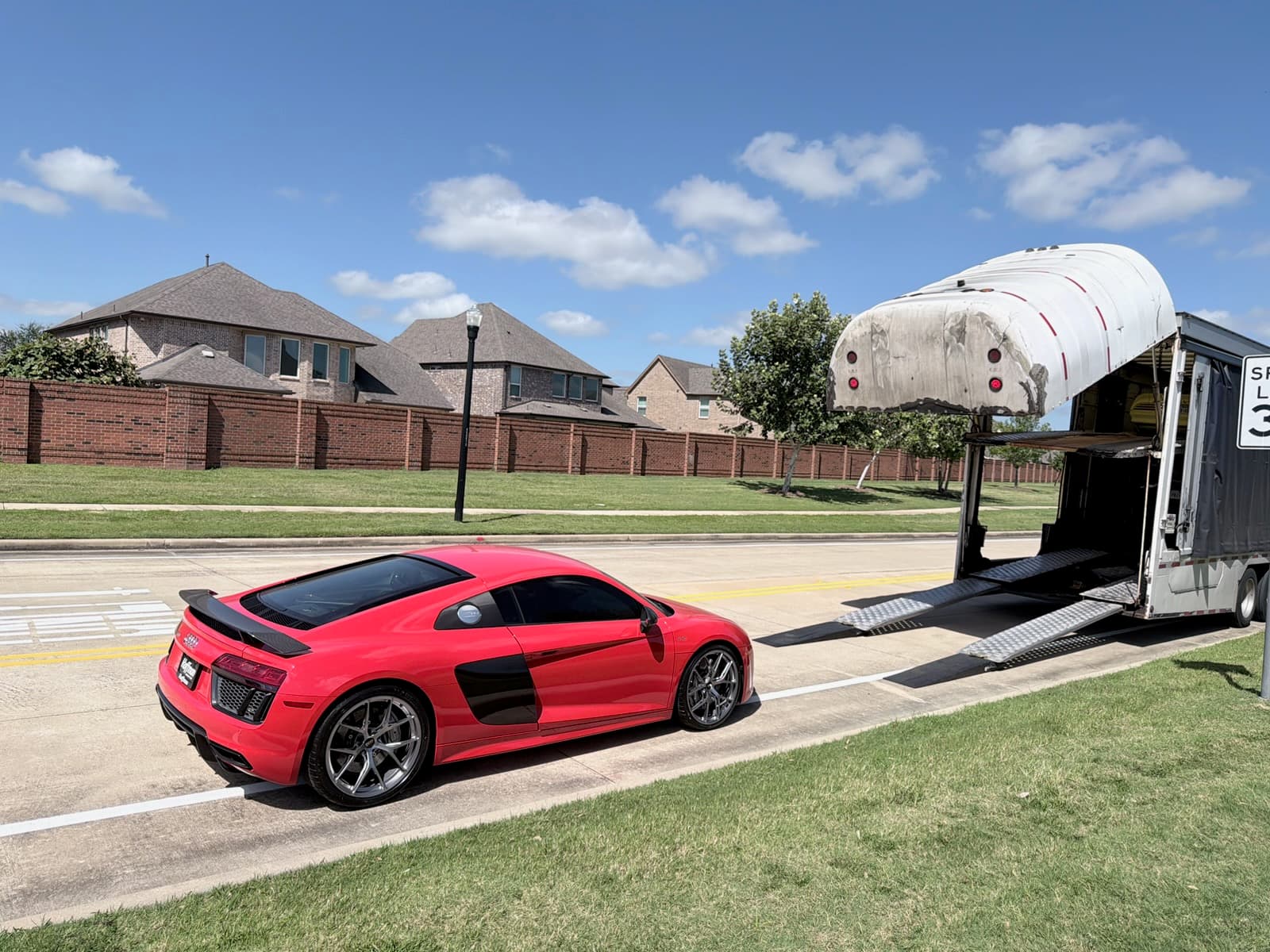 Red Audi R8 parked beside an enclosed auto transport trailer