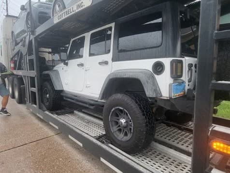 Jeep Wrangler secured on a multi-car open carrier ahead of departure from Houston, TX