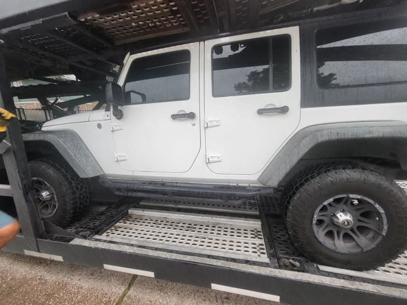 White Jeep Wrangler loaded on an open auto transport carrier