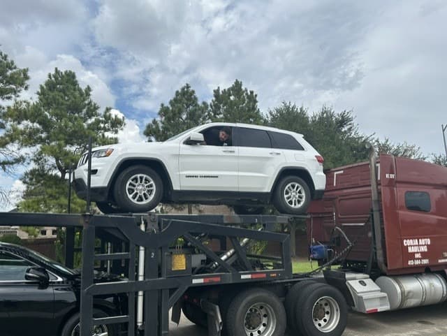 White Jeep Grand Cherokee loaded on the upper deck of an open multi-vehicle carrier in Katy, TX
