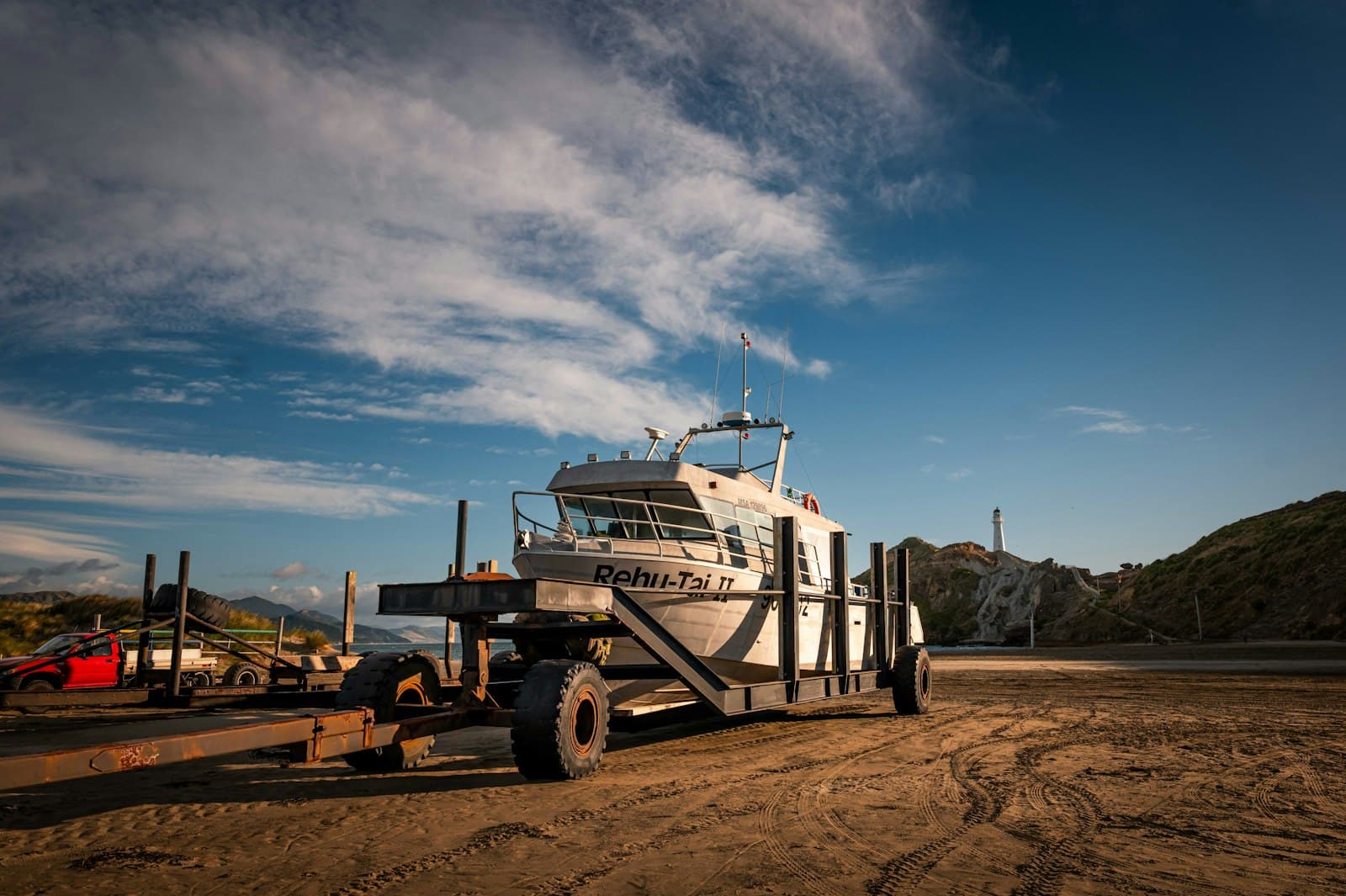 Large vessel loaded on a heavy-duty trailer near a coastal lighthouse