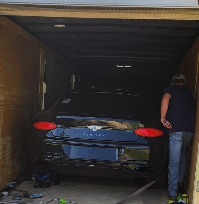 Black Bentley loaded inside an enclosed auto transport trailer with a handler checking the vehicle