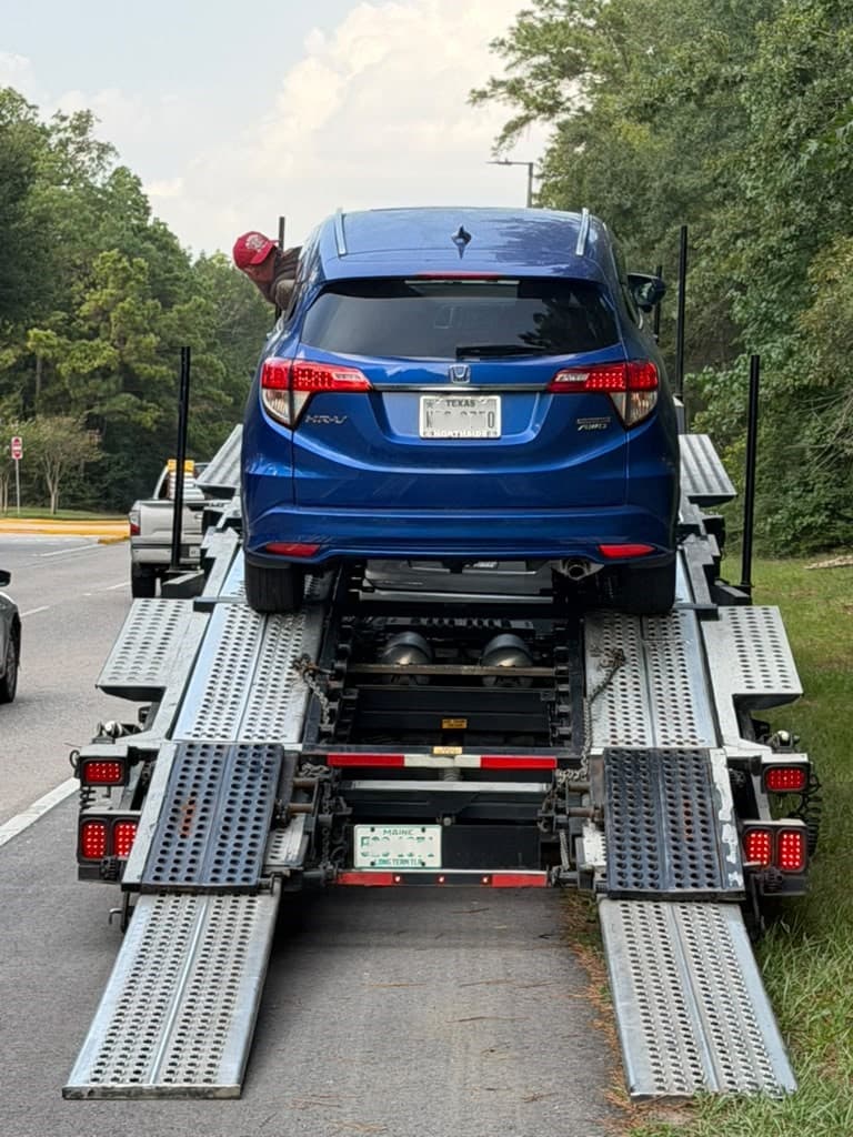 A blue SUV being loaded onto the ramps of an open, multi-car auto transport trailer