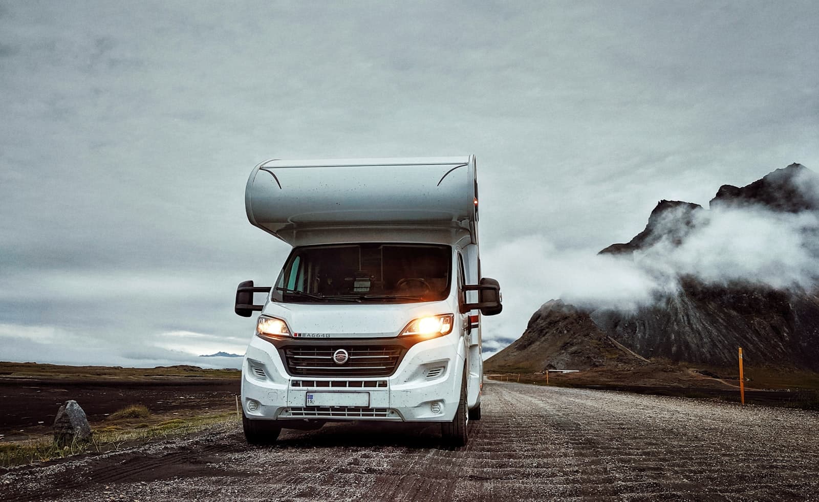 Class C motorhome parked on a gravel road with mountains in the background